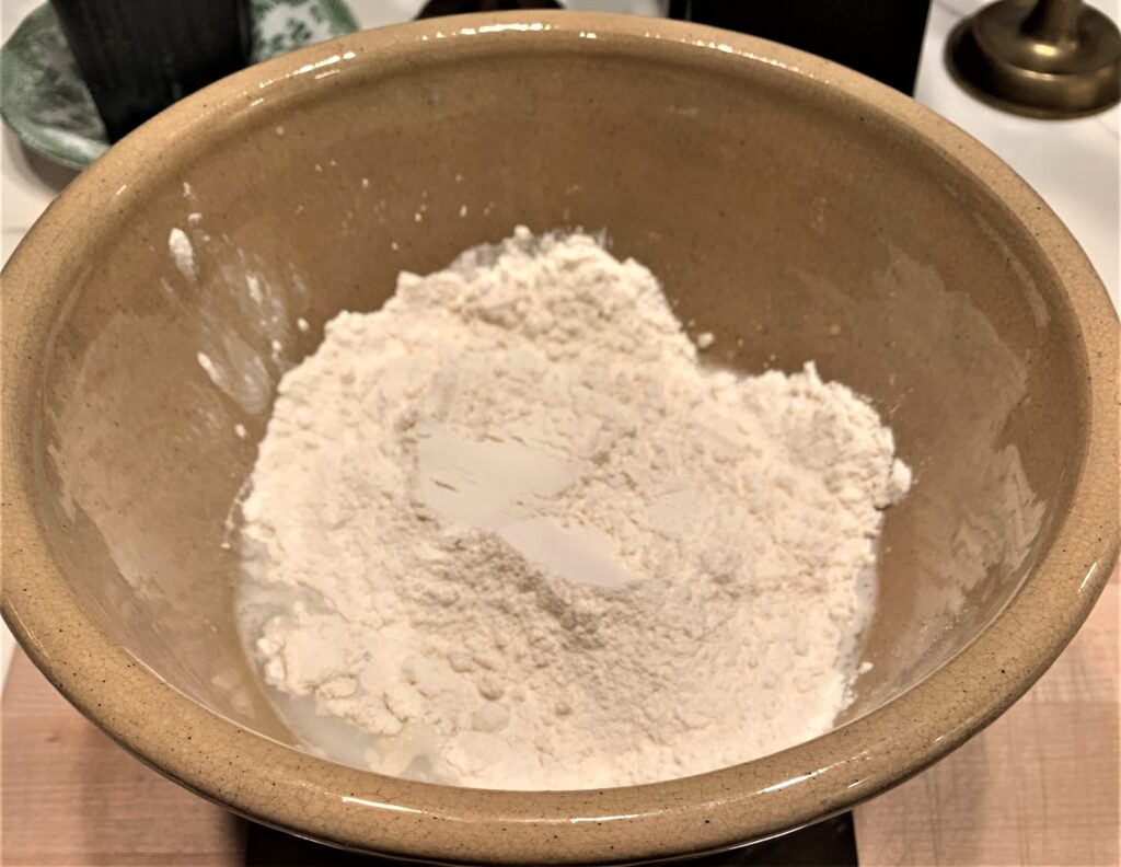 120g flour added to water and starter mixture in a bowl on top of a digital scale