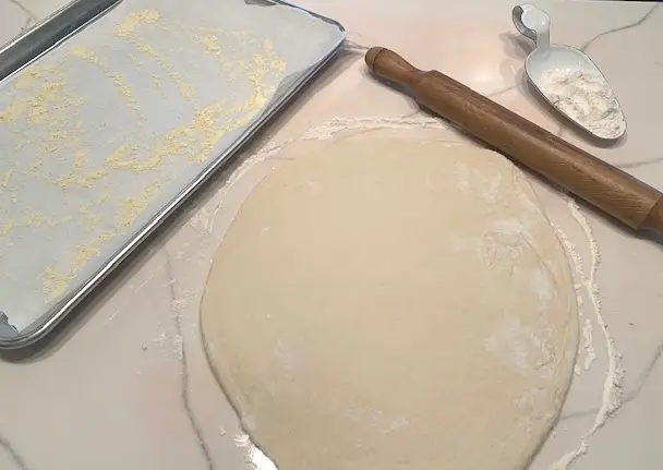 sourdough rolled out with a rolling pin on a floured surface. sheet pan cover with parchment paper and sprinkled with cornmeal