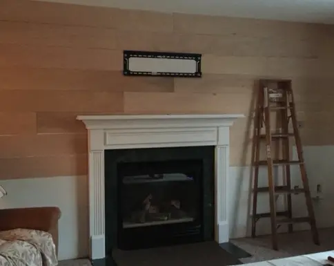 plywood planks attached to wall with ladder and white fireplace mantel