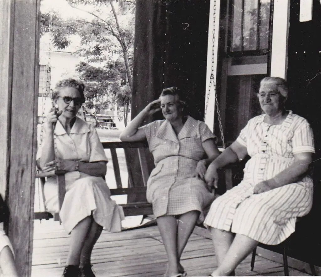 three women sitting on a swing on a front porch