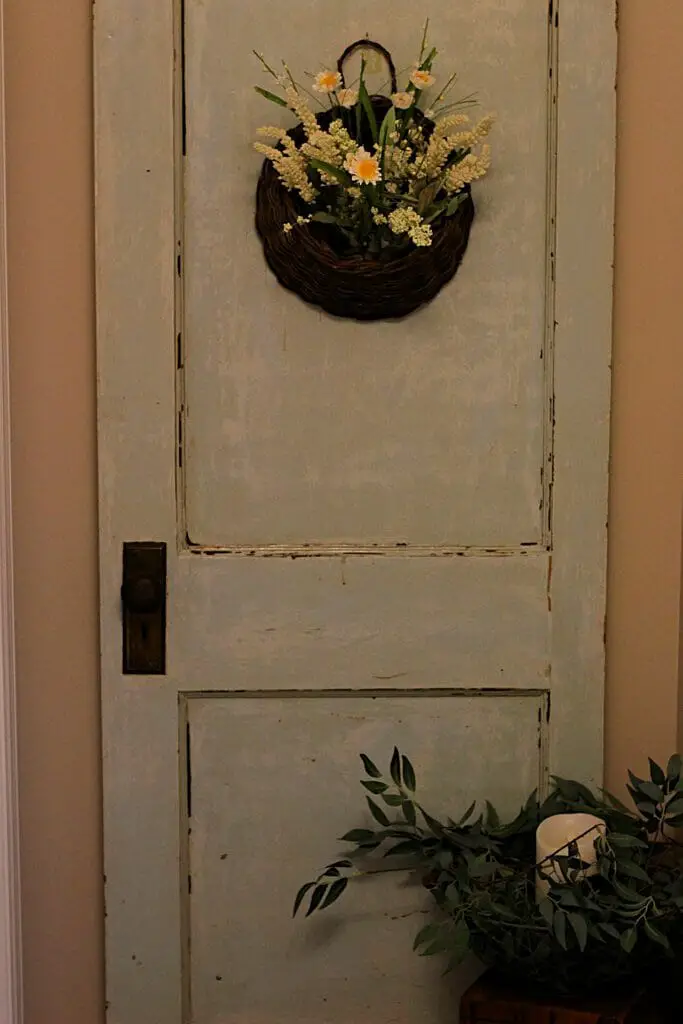 old door hung on a wall in blue color with basket and fake flowers hung on door