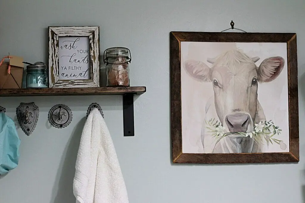 blue wall with wood shelf, key towel hooks and picture of a cow on wall for a small bathroom farmhouse style spa makeover