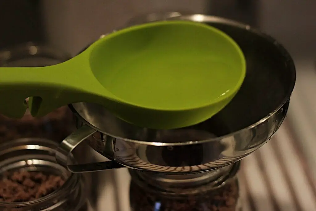 green ladle pouring boiling water into canning jar