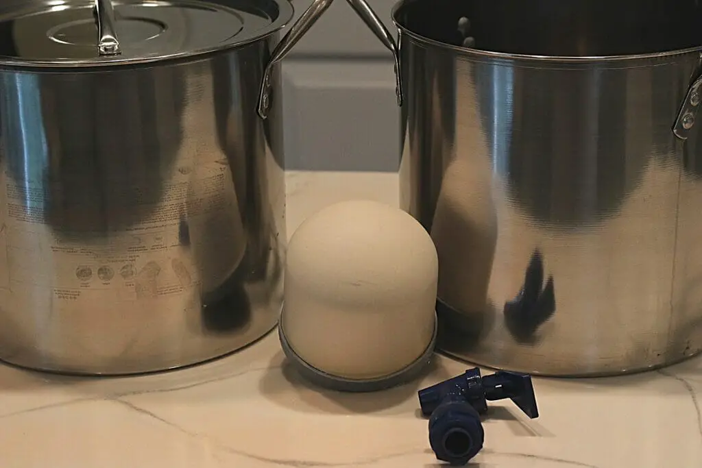 components of a berkey-style water filtration system: two stainless steel pots, ceramic filter and spigot