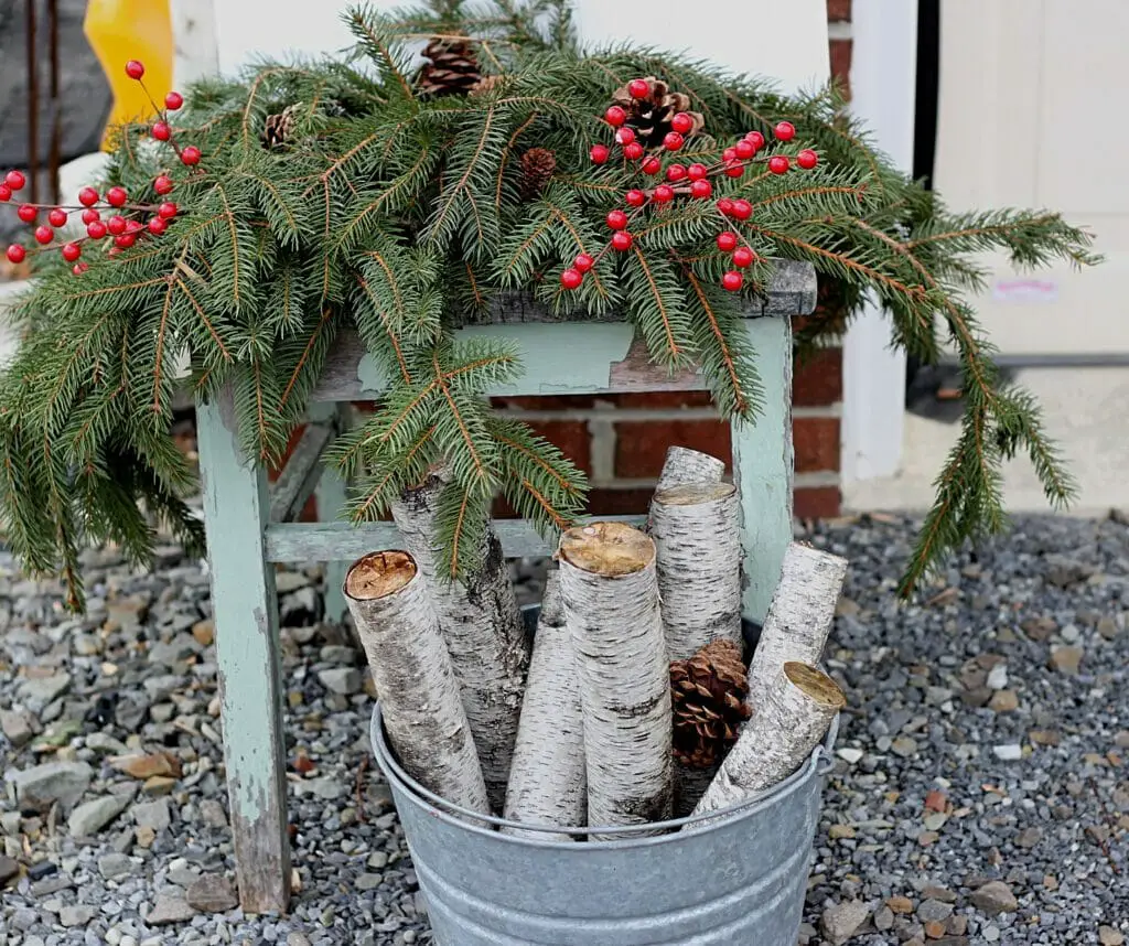 pine branches, faux red berry picks, and metal bucket filled with wood logs