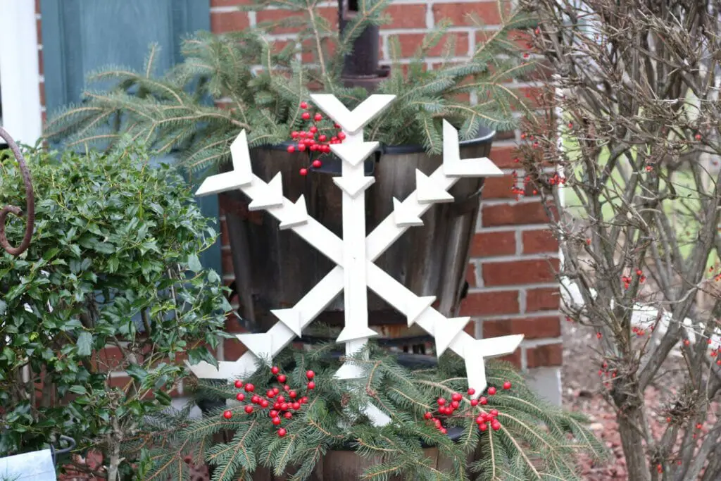 barrel planter with pine branches and wooden snowflake creating a simple natural winter decor