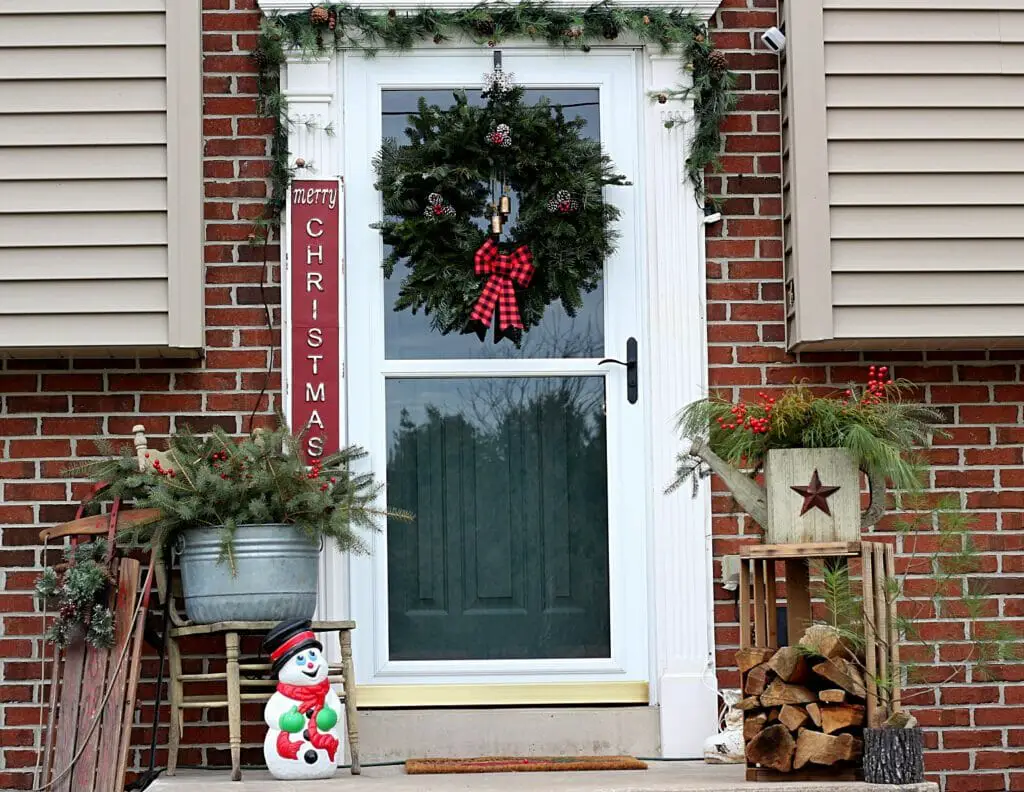 Front stoop decorated with natural pine and spruce branches, logs, blow mold and garland