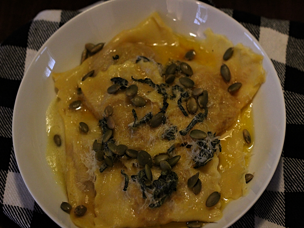 finished bowl of pumpkin ravioli with brown butter sage sauce topped with parmesan cheese and pumpkin seeds