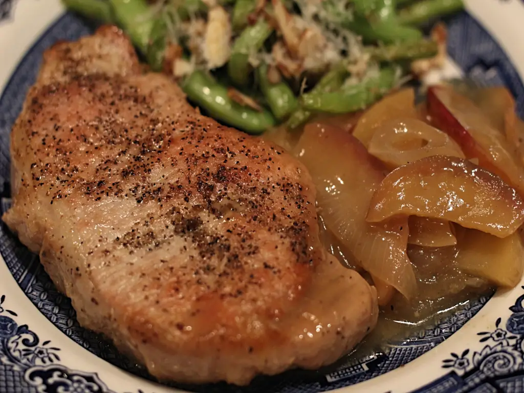 plate with pork chop, apples onions and cider sauce with a side of sauteed green beans