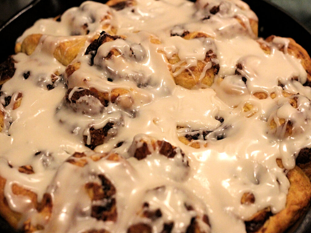 cast iron skillet with sourdough pumpkin cinnamon rolls and icing